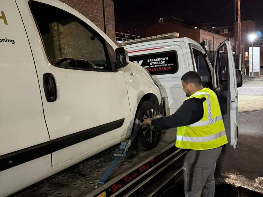 blue van secured on KMX recovery truck during nighttime roadside vehicle recovery service in wet conditions