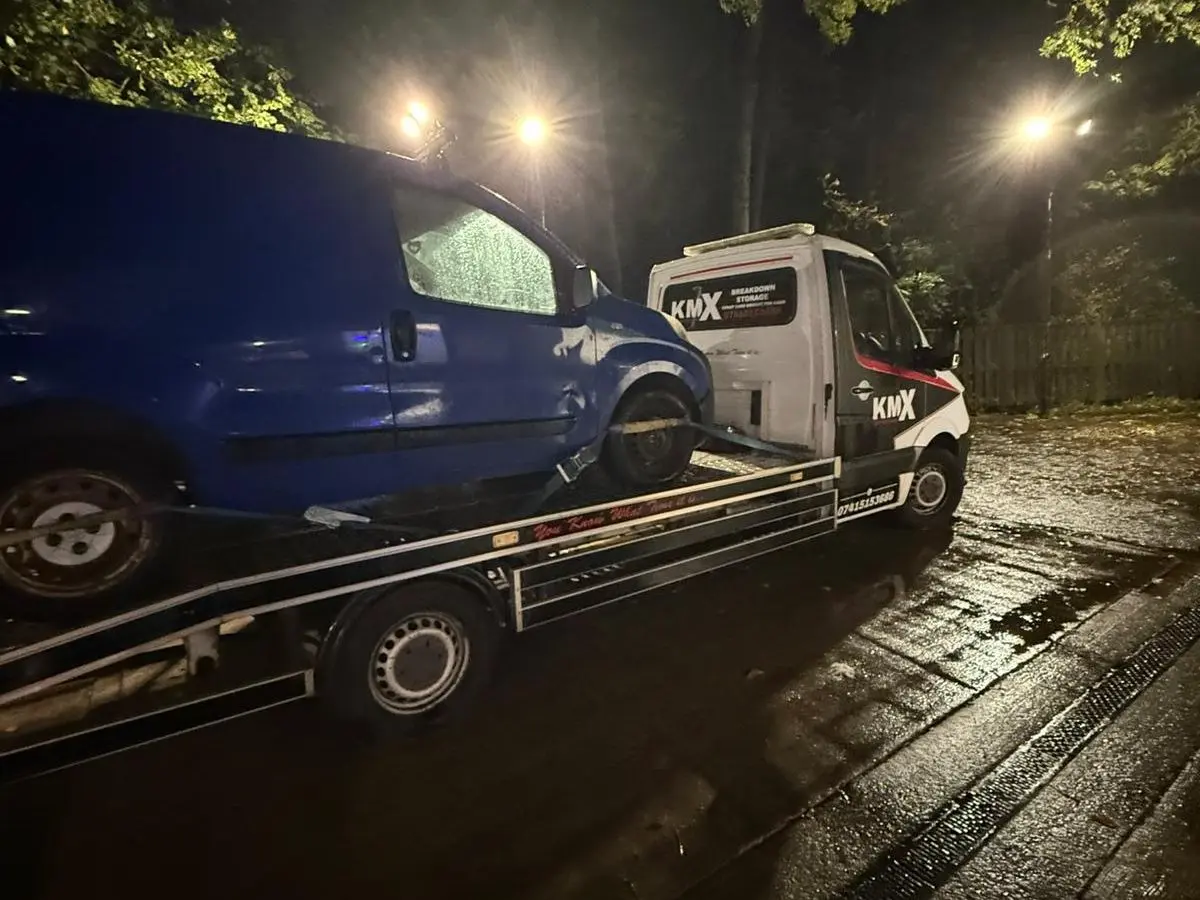 recovery operator securing white van on KMX flatbed truck using straps during vehicle recovery service