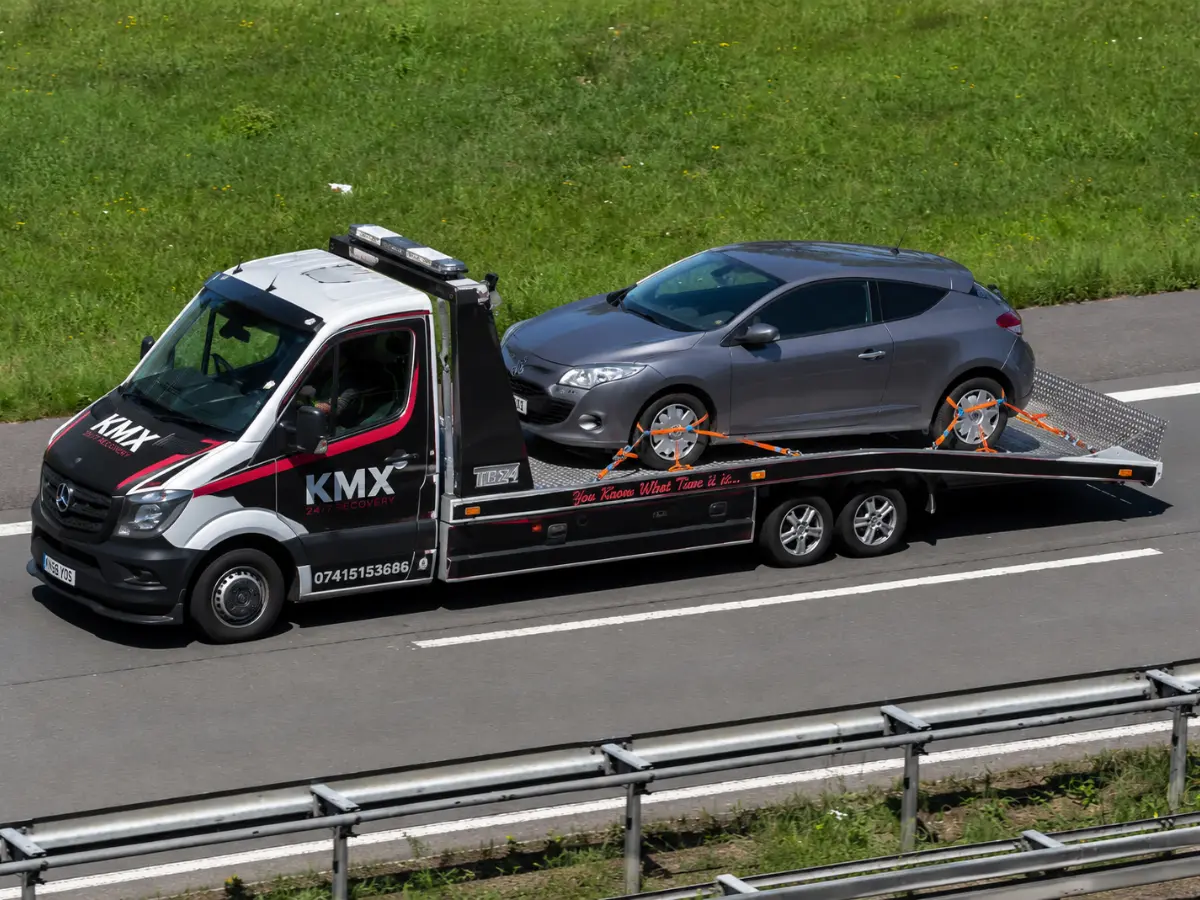 KMX recovery truck transporting a broken-down car as part of a 24/7 vehicle recovery service.