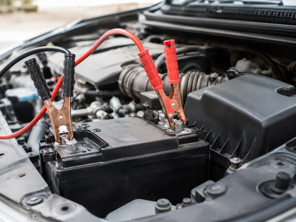 Close up of red and black jump leads connected to a car battery during a safe jump start.
