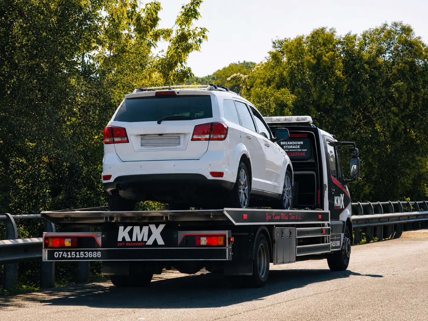 KMX recovery truck transporting a white SUV during a professional car recovery in Bury.