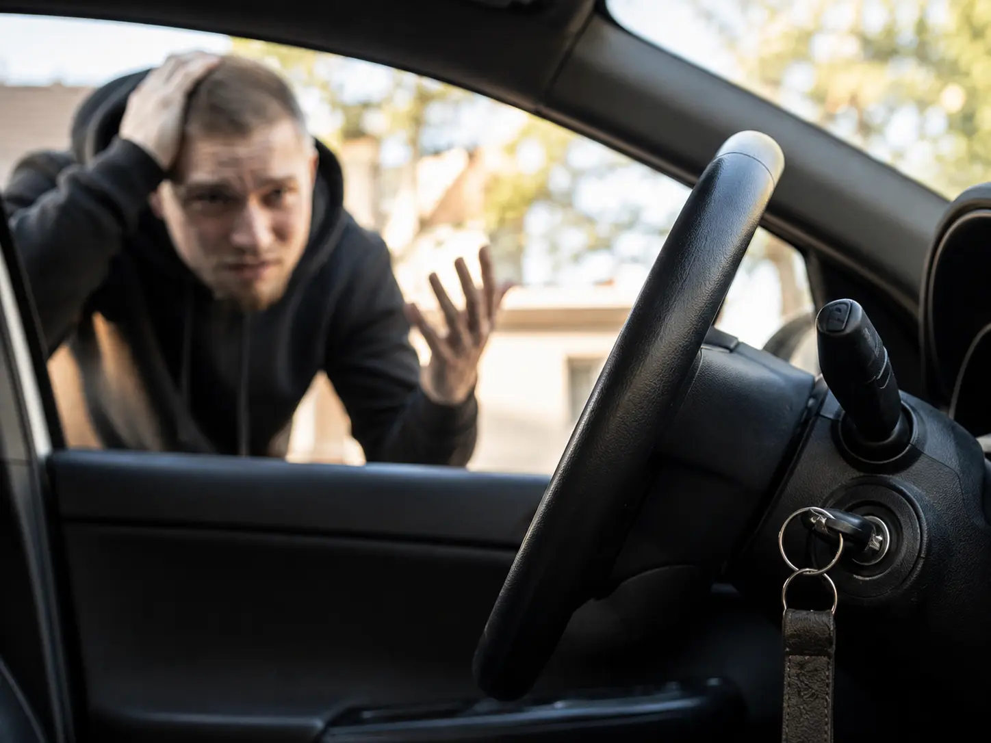 Frustrated driver looking through a car window at keys left inside the ignition.